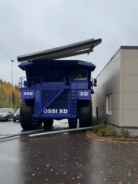Valtava sininen kaivosauto seisoo pikaruokalan drive-in-kaistalla, ja murskautunut katos lepää sen keulan päällä.