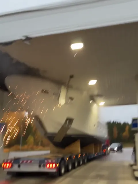 Valkoinen superjahti rekan lavalla on iskeytynyt huoltoaseman katokseen, ja kipinät lentävät.
