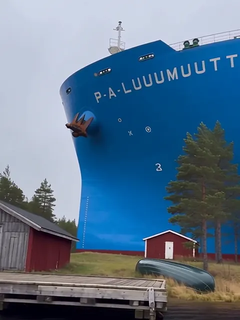 Sinisen jäänmurtajan valtava keula rannassa harmaan venevajan ja mökkilaiturin vieressä.
