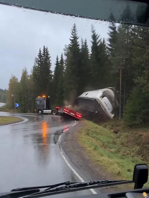 Rekan perävaunu on kaatunut liikenneympyrässä, ja valkoinen superjahti vierii metsänreunaan.