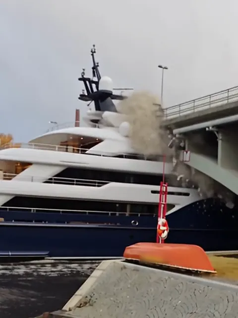 Sininen superjahti törmää betoniseen kaarisiltaan, ja törmäyskohdasta nousee pölyä.