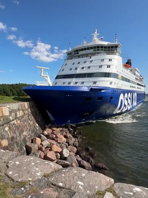 Sinivalkoinen jättilaiva on ajanut keulallaan Suomenlinnan rantakallioille.